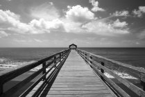 Black and white picture of wooden pier over sea water under cloudy sky during daytime — Stock Photo