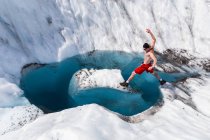 Homem seminua em shorts saltando sobre lagoa de água cercada por neve e gelo — Fotografia de Stock