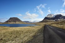 Un camino de asfalto a lo largo de la costa con montañas nevadas, península de Snaefellsnes; Islandia - foto de stock