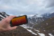 Mão segurando smartphone na mão com montanhas no fundo — Fotografia de Stock