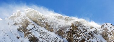 Close-up de um pico de montanha coberto de neve com neve soprando e céu azul, Peter Lougheed Provincial Park; Alberta, Canadá — Fotografia de Stock