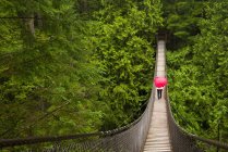 Donna con un ombrello a forma di cuore rosso che attraversa il Lynn Canyon Suspension Bridge, North Vancouver; Vancouver, Columbia Britannica, Canada — Foto stock