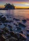 Золотой солнечный свет, освещающий облака вдали и мокрые камни вдоль короткой линии; Ванкувер, Британская Колумбия, Канада — стоковое фото
