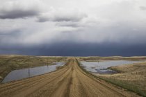 Chemin de gravier se dirigeant vers un ciel orageux dans le sud-ouest de la Saskatchewan ; Val Marie, Saskatchewan, Canada — Photo de stock