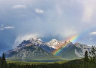 Um arco-íris emerge entre picos de montanha acidentados durante uma forte tempestade de chuva; Banff, Alberta, Canadá — Fotografia de Stock