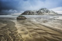 Пейзаж с пересеченными горами и песком вдоль береговой линии под облачным небом; Остланд, Норвегия — стоковое фото