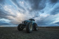 Tractor parked in a field under a dramatic sky at sunset; Val Marie, Saskatchewan, Canada — Stock Photo