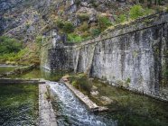 Eine abgenutzte Steinmauer mit Kaskadenwasser entlang der Bucht von Kotor; Kotor, Montenegro — Stockfoto