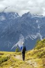 Caminhante feminina ao longo da trilha alpina com montanhas cobertas de nuvens ao fundo, Sesto, Bolzano, Itália — Fotografia de Stock
