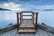 A wooden viewing platform at the end of a dock looks out to a ship on the tranquil ocean; Vancouver, British Columbia, Canada — Stock Photo