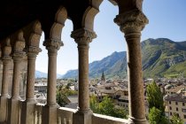 Palace stone columns frames an alpine village in the background with mountains and blue sky; Trento, Trento, Italy — Stock Photo