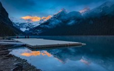 Picos de las Montañas Rocosas iluminados por la luz del sol y reflejados en el Lago Louise; Lago Louise, Alberta, Canadá - foto de stock