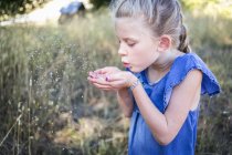 Молода дівчина дме маленьке зерно з забитих рук у повітря — стокове фото