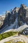 Escursionista femminile su sentiero con valle sottostante contro una catena montuosa frastagliata e cielo azzurro, Sesto, Bolzano, Italia — Foto stock