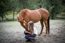 A teenage girl crouching down to talk to and care for her horse; British Columbia, Canada — Stock Photo