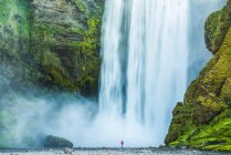 Homem em pé na base da cachoeira Skogafoss; Islândia — Fotografia de Stock