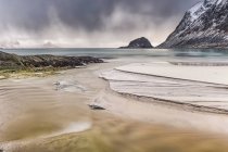 Un paisaje con montañas escarpadas y arena a lo largo de la costa bajo un cielo nublado; Nordland, Noruega - foto de stock