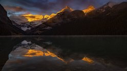 Luce solare dorata che illumina le cime delle montagne e si riflette nelle tranquille acque del Lago Louise, Banff National Park; Alberta, Canada — Foto stock