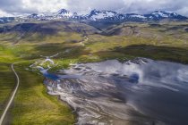 El camino serpenteando alrededor de la península Snaefellsness con un río trenzado que corre hacia el océano; Islandia - foto de stock