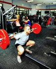 A young man doing squat lifts during his weight resistance training at a fitness facility — Stock Photo