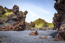 Coloridas formaciones rocosas de lava diseminadas por la playa de arena negra en el Parque Nacional Snaefellsjokull, Islandia - foto de stock