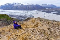 Женщина-туристка в теплой одежде на горе с видом на ледниковое озеро и долину внизу в Национальном парке Ватнайокулл, Исландия — стоковое фото