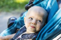Cute little baby girl sitting in a stroller and looking at side — Stock Photo