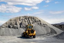 Large wheel loader in front of a gravel pile in the mountain landscape — Stock Photo