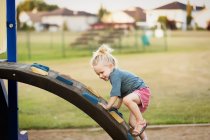 Young girl with blond hair playing in a playground and climbing up a rock ladder — Stock Photo