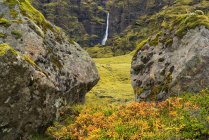 Ein großer namenloser Wasserfall, der von großen Steinen entlang der Südküste von Island eingerahmt ist; — Stockfoto