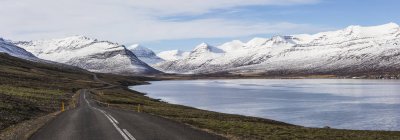 The road running along a fjord on Iceland 's East Fjord region seen heading into the mountains; Iceland — стоковое фото