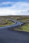 Leere Straße schlängelt sich durch die zerklüftete Landschaft Hügel, Island — Stockfoto