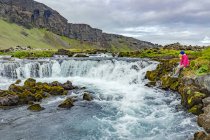 Una excursionista posa para una foto en el borde de una cascada; Islandia - foto de stock