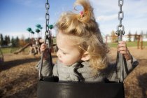 Cute young girl with funny face while swinging in a playground — Stock Photo