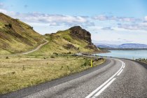 Largo camino sinuoso que conduce a las colinas en Islandia, donde las carreteras pavimentadas abiertas conducen a través del paisaje volcánico a las vistas de todo el país, Islandia - foto de stock