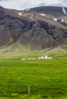 Большая фермерская собственность, окруженная огромными полями перед вулканическими склонами, Исландия — стоковое фото