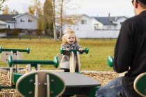 Carino giovane ragazza giocare su altalena con papà in parco giochi — Foto stock