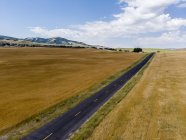 Estrada em linha reta através do campo com campos dourados de terras agrícolas em ambos os lados, Mendon, Utah, EUA — Fotografia de Stock