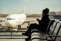 Passagierin sitzt im Flughafenterminal mit ihrem Smartphone, Peking Hauptstadt internationaler Flughafen, Peking, China — Stockfoto