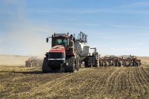 Traktor zieht eine Sämaschine, sät ein Feld mit blauem Himmel und Wolken im Hintergrund — Stockfoto