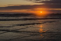 O sol se põe na praia e reflete sobre a água com vista para o horizonte, Tolovana Park, Oregon, EUA — Fotografia de Stock