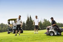 Группа гольфистов, один из которых инвалид с мобильным устройством помощи, наблюдает, как долгий путь, как он делает свой путь вниз по фарватеру, Эдмонтон, Альберта, Канада — стоковое фото