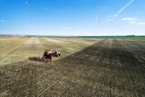 Trator puxando um semeador de ar, semeando um campo com céu azul na distância — Fotografia de Stock