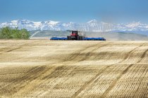 Trattore tirando un cercatore d'aria, seminando un campo con montagne e cielo blu sullo sfondo — Foto stock