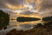 El sol sale a través de un cielo nublado sobre las Islas Broken Group frente a la costa oeste de la isla de Vancouver, Pacific Rim National Park Reserve, Columbia Británica, Canadá - foto de stock