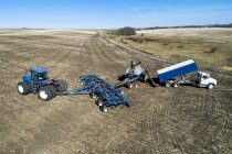 Вид с воздуха фермера, заполняющего бункер с сеялкой воздуха грузовиком в поле с голубым небом на заднем плане — стоковое фото