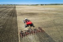 Tractor pulling an air seeder, seeding a field with blue sky in the distance — Stock Photo