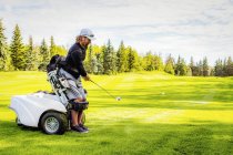Інвалідів гольфіст водіння м'яч на гольф зелений і за допомогою спеціалізованих гольф допомоги моторизованих гідравлічні інвалідного візка, Едмонтон, Альберта, Канада — стокове фото