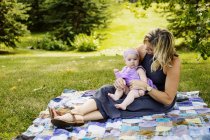 Madre y su hija bebé sentadas en una manta de picnic - foto de stock
