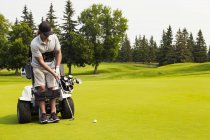 Інвалідів гольфіст надягаючи м'яч гольф зелений і за допомогою спеціалізованих гольф допомоги моторизованих гідравлічні інвалідного візка, Едмонтон, Альберта, Канада — стокове фото